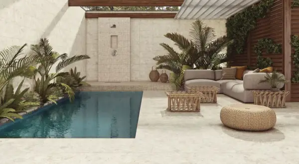 Piscina y zona lounge con sofás y mesas bajas, ducha exterior y plantas exuberantes. El suelo y las paredes lucen un elegante microcemento exterior.