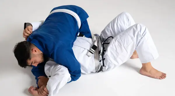 Två män i judodräkter brottas på golvet. En blå och en vit dräkt, en kamp mellan judo vs bjj.