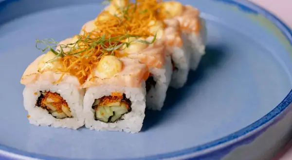 Rolka sushi z łososiem i warzywami na niebieskim talerzu. Czy w ciąży można jeść sushi? To pytanie nurtuje wiele przyszłych mam.