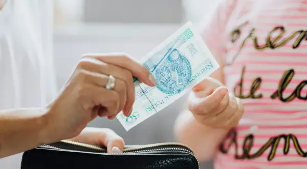 Dłoń trzyma banknot 50 zł nad czarnym portfelem.