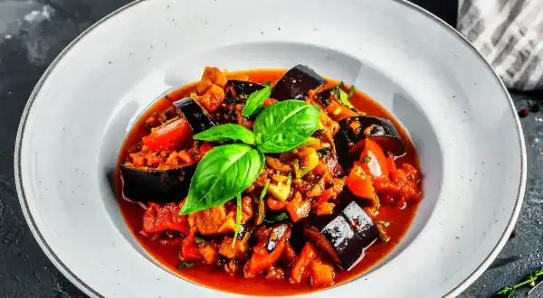 Un plat de ratatouille au four, garni de basilic frais, avec des aubergines, des tomates et d'autres légumes mijotés dans une sauce savoureuse.