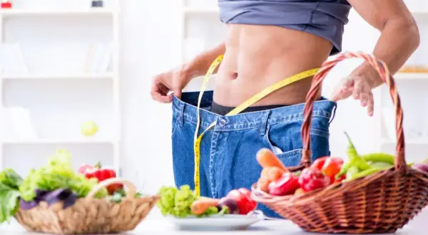 Uomo con jeans larghi e metro, simbolo di successo con dieta ipocalorica. Cesti di verdura fresca in primo piano.