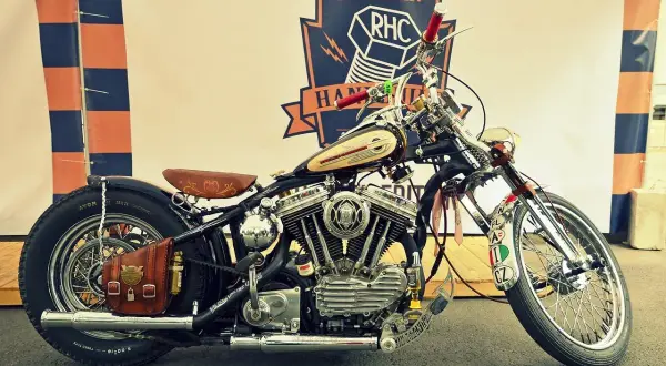 Customowy motocykl z chromowanymi elementami, skórzanym siedzeniem i sakwą, na tle baneru Russian RHC.
