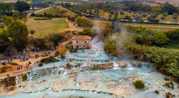 Cascate naturali con acqua azzurra e gente che si rilassa, un vero spettacolo di arte terme in un paesaggio collinare.