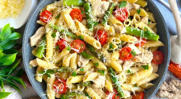 Makaron penne z kurczakiem, szparagami i pomidorkami koktajlowymi, posypany serem.