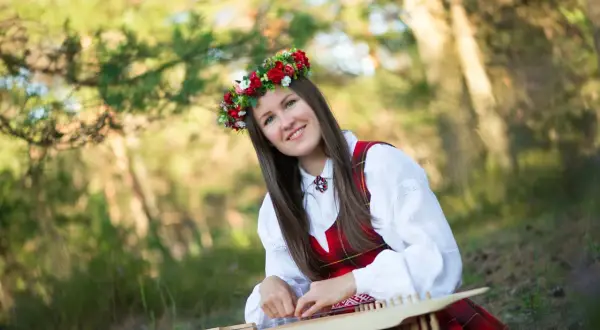 Uśmiechnięta kobieta w wianku i tradycyjnym stroju gra na cymbałach, tworząc piękną polską muzykę ludową.