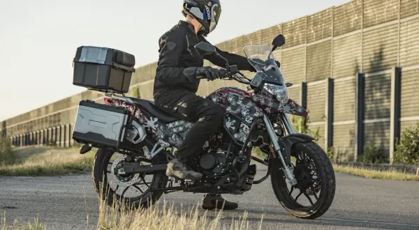 Motocyklista w kasku i czarnej kurtce siedzi na motocyklu Junak RX One 125 z kuframi.