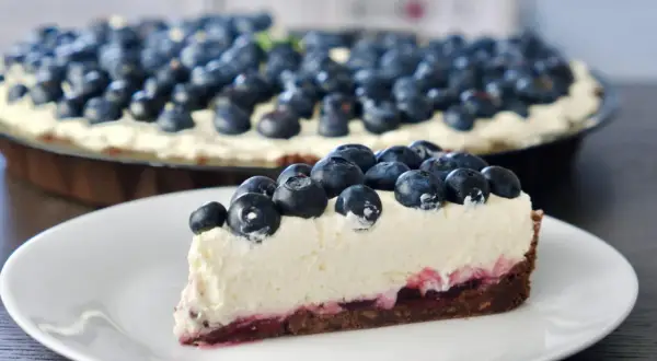 Kawałek tarty z jagodami i kremem mascarpone na białym talerzyku.
