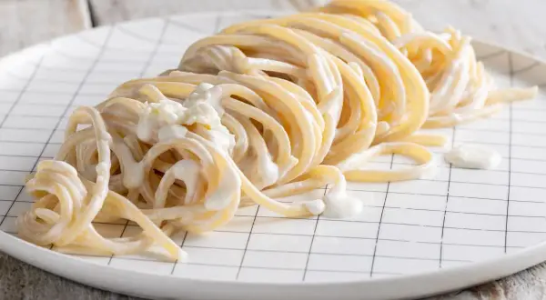 Un piatto di spaghetti avvolti in una cremosa salsa alla panna, serviti su un piatto bianco a quadretti neri.
