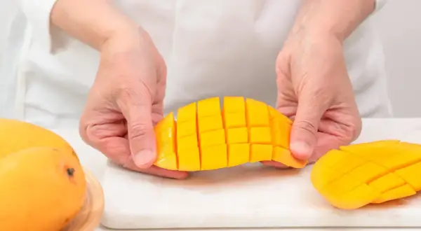 Ręce kroją mango na kostki. Czy koty mogą jeść mango? To pytanie nurtuje wielu właścicieli.