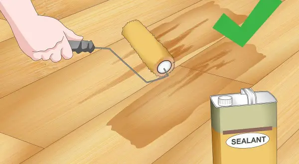 Application d'un scellant sur un plancher en bois. Le rouleau laisse une trace humide, signe que le produit pénètre bien le bois, éliminant toute rayure.