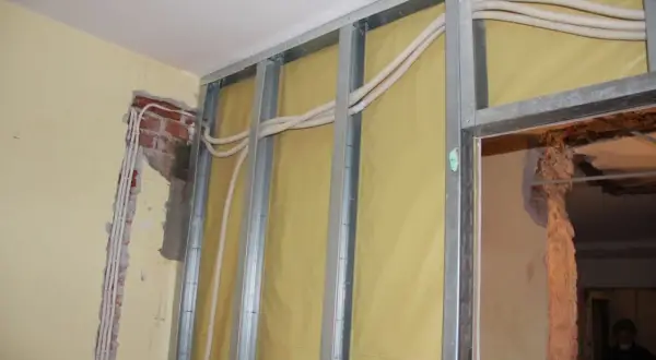 Nowa instalacja elektryczna bez kucia ścian. Widoczne profile metalowe, izolacja i nowe przewody w peszlach.