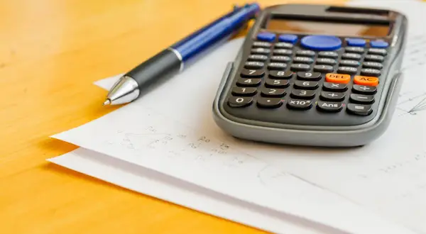 Kalkulator i długopis na kartkach z zadaniami. Czy na egzaminie ósmoklasisty można mieć kalkulator? Sprawdź zasady!