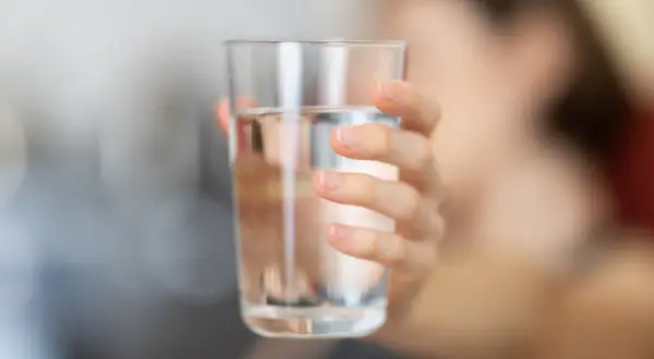 Main d'une personne tenant un verre d'eau. L'eau calcaire peut affecter la santé, mais une hydratation adéquate est essentielle.