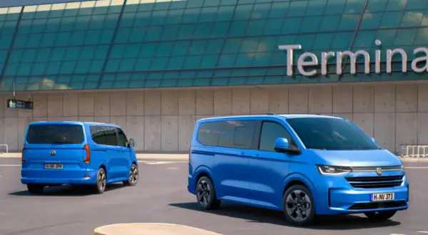 Dwa niebieskie Volkswageny Caravelle stoją przed budynkiem terminala lotniska.