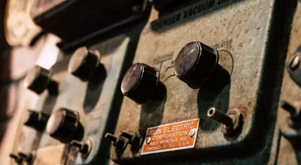 Stare pokrętła na panelu urządzenia Sun Electric Corporation. Widać napis "CONDENSER VACUUM REGULATOR" i adres firmy. To może być część starego warystora.