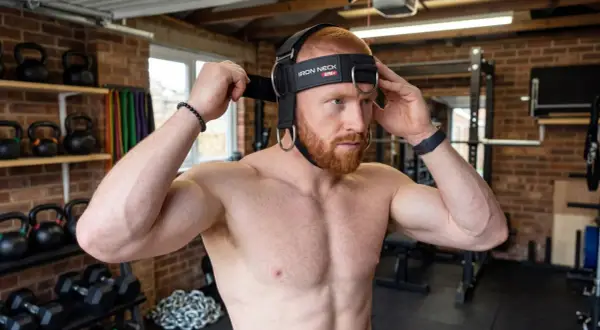 Man adjusting a neck training harness, ready for a workout. This image captures the start of his neck training journey.