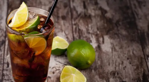 Erfrischender Cuba Libre mit Limettenspalten und Eiswürfeln auf rustikalem Holz. Das Cuba Libre Rezept ist einfach und lecker.