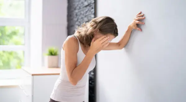 Frau lehnt sich an Wand, hält sich die Augen. Sie fragt sich, was tun bei Schwindel.