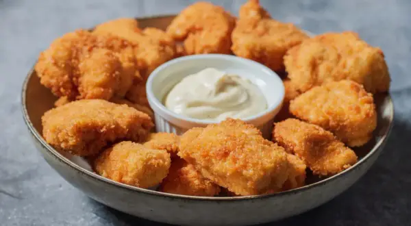 En skål med gyllene, krispiga chicken nuggets och en liten skål med krämig dipp. Perfekt för en snabb och god måltid.