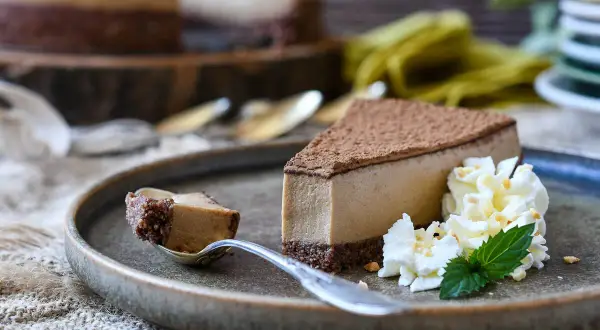 Deliciosa tarta de café con queso Philadelphia, cubierta de cacao y acompañada de nata montada y menta.
