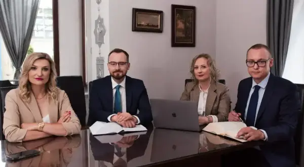 Cztery osoby w strojach biznesowych siedzą przy stole w sali konferencyjnej.