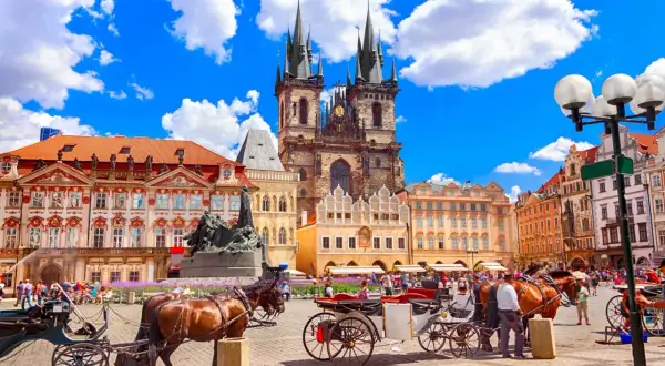 Rynek w Pradze z kościołami, kamienicami i dorożkami konnymi.
