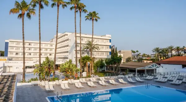 Basen i leżaki przy hotelu TUI Suneo Santa Ponsa. Palmy i biały budynek hotelowy na tle błękitnego nieba.