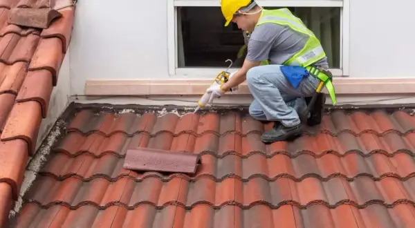 A roofer applies sealant to a shingle roof detail, ensuring a watertight seal around the window.