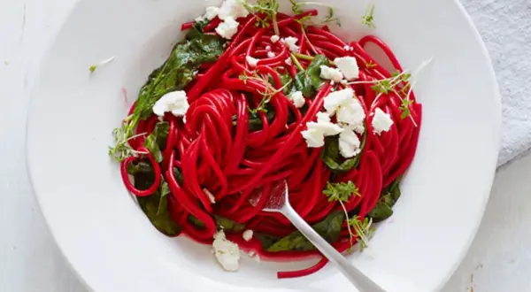 Rote-Bete-Spaghetti mit Spinat, Feta und Kresse auf einem Teller.