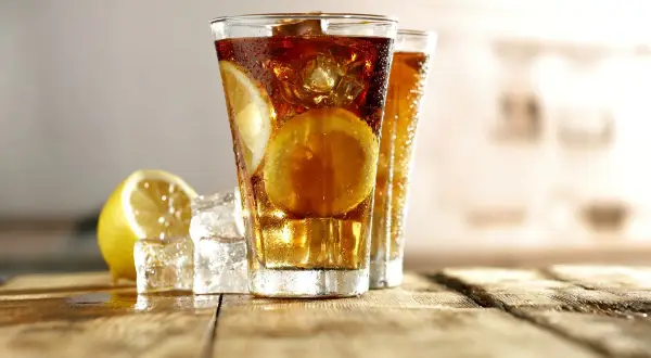 Dwa orzeźwiające drinki Long Island Ice Tea z plasterkami cytryny i kostkami lodu na drewnianym blacie.