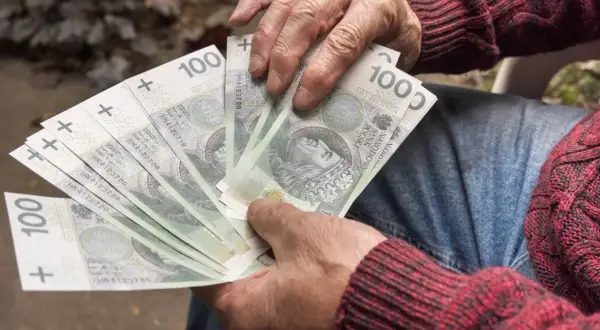 Dłonie trzymające banknoty 100 zł. Zastanawiasz się, ile wynosi renta na kręgosłup?