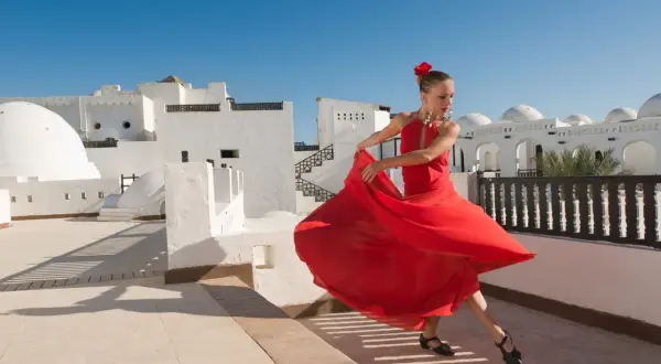 Bailarina con vestido rojo gira con gracia, evocando la pasión de los flamencos de Jerez bajo un cielo azul.