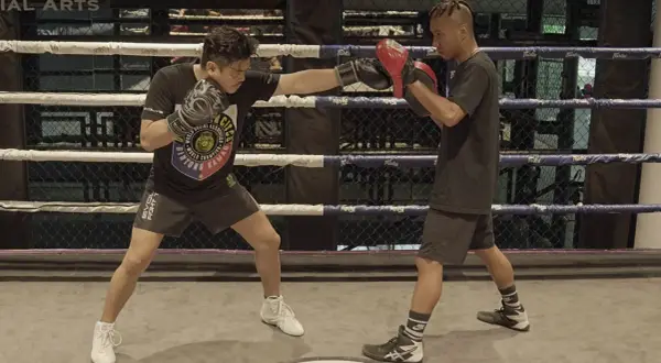 A boxer throws a jab punch during training in a boxing ring.