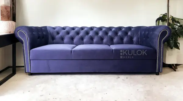 Elegancka, granatowa kanapa chesterfield z pikowanego welwetu, ozdobiona srebrnymi pineskami.