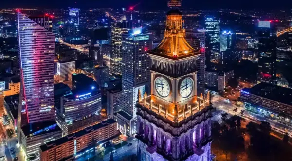 Wieżowiec z zegarami i nowoczesne budynki tworzą magiczny krajobraz warszawa nocą.
