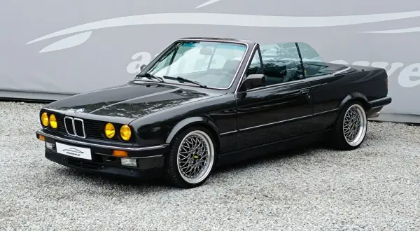 Czarny kabriolet BMW E30 z żółtymi światłami i felgami BBS. Klasyk na drodze.