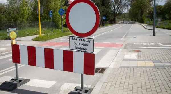 Znak B1 zakazu ruchu z tabliczką "Nie dotyczy pojazdów budowy" na tle drogi z pasami.
