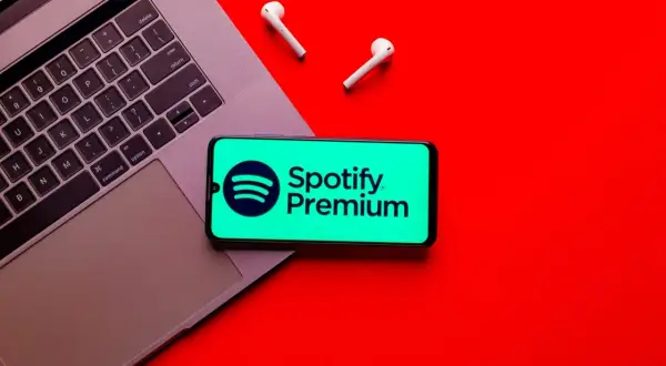 Telefon z logo Spotify Premium na tle laptopa i słuchawek bezprzewodowych.