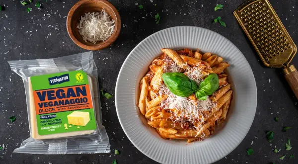 Talerz penne z sosem, opakowanie wegańskiego parmezanu i złota tarka.
