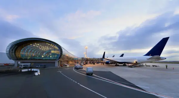Flugzeuge am Flughafen Paris warten auf den Abflug. Ein modernes Terminalgebäude mit Glasfassade spiegelt den Himmel.