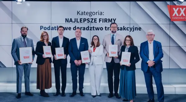 Grupa osób w garniturach i sukienkach odbiera dyplomy na tle ekranu z napisem "Kategoria: Najlepsze Firmy".