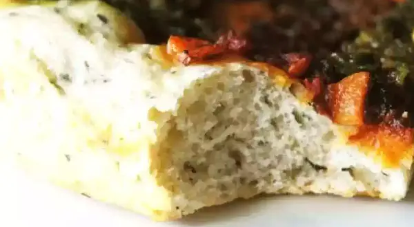 Gros plan sur une tranche de pâte à pizza sans gluten moelleuse, garnie de tomates et d'herbes.