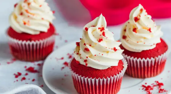 Drei rote Samt-Cupcakes mit cremiger weißer Glasur und roten Krümeln.