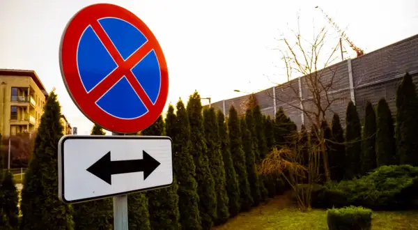 Znak zakaz parkowania z tabliczką wskazującą kierunki.