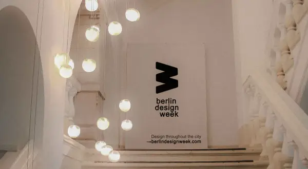 Eine Treppe mit Hängeleuchten und einem Banner für die **Berlin Design Week**.