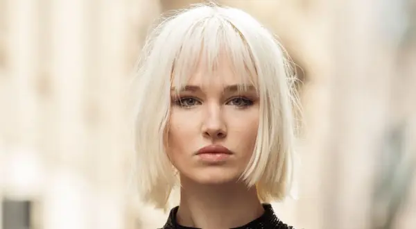 Mujer joven con un moderno corte bob rubio platino y maquillaje sutil.