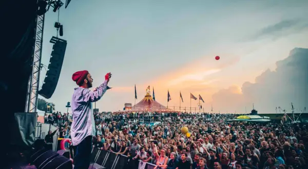 Bühnenkünstler wirft roten Ball in die Menge beim Watt en Schlick Festival Dangast. Ein Meer aus Menschen feiert unter dem Abendhimmel.