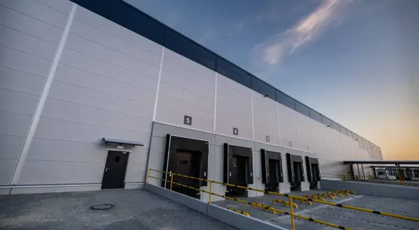 Nowoczesne centrum logistyczne InPost z rampami załadunkowymi i drzwiami, pod błękitnym niebem.