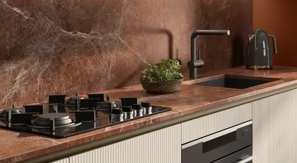 Piano cottura a gas su top in marmo rosso, con lavello nero, rubinetto moderno e bollitore Smeg. Le cucine con pavimento cotto hanno un fascino rustico.